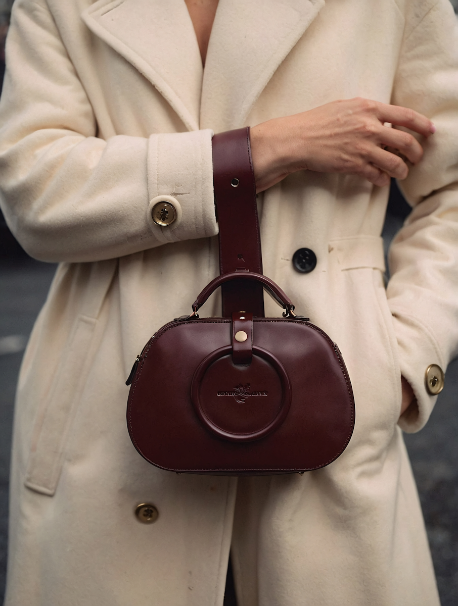 Beżowy płaszcz i burgundowa torebka, kobieta trzyma rękę w kieszeni